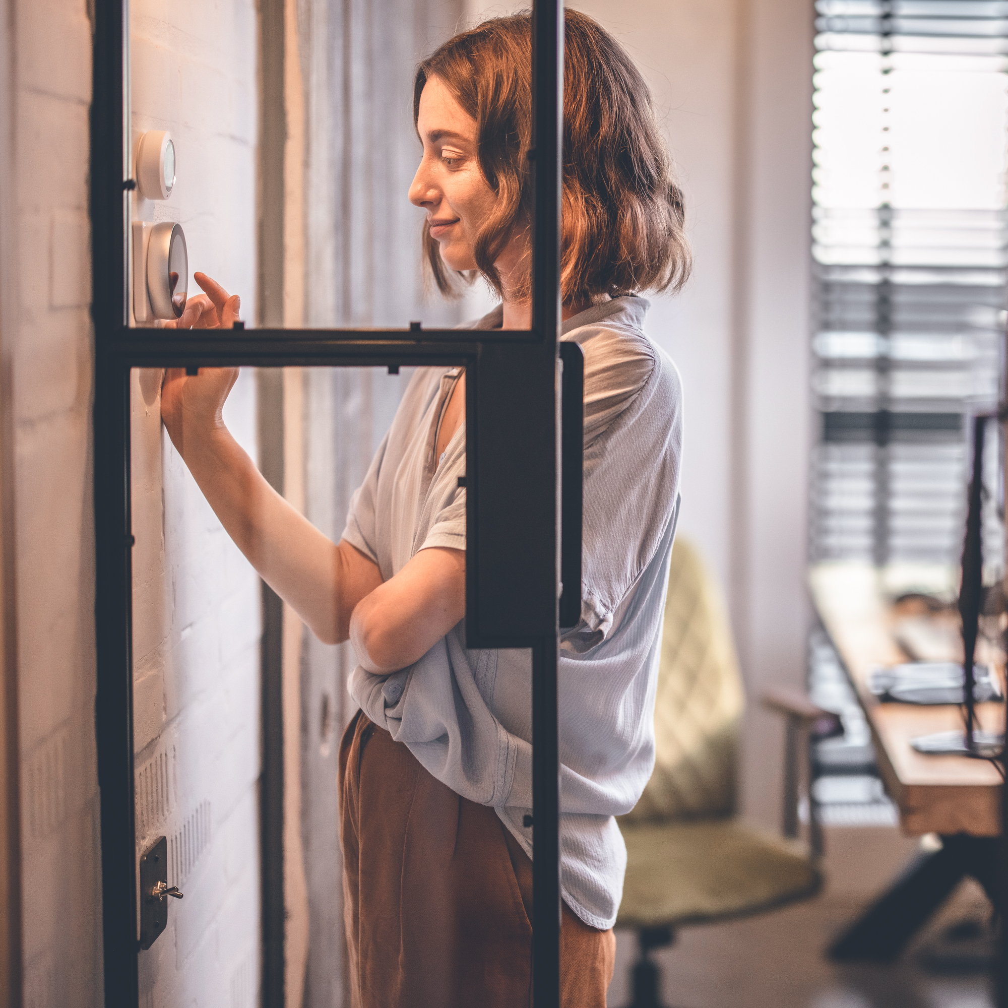 Young woman controlling room temperature with a smart thermostat at home.