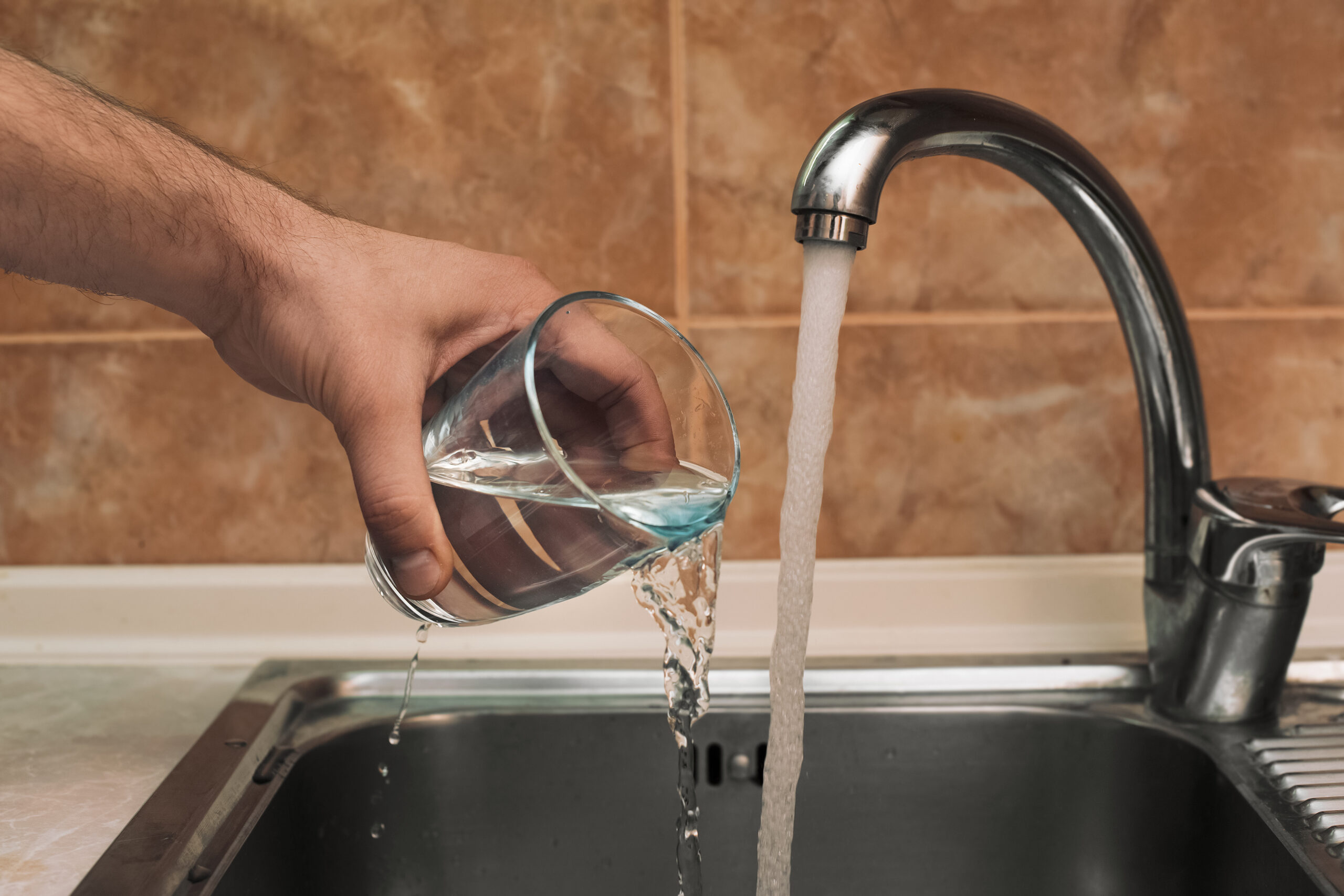 Man pours water from a glass in the kitchen sink.