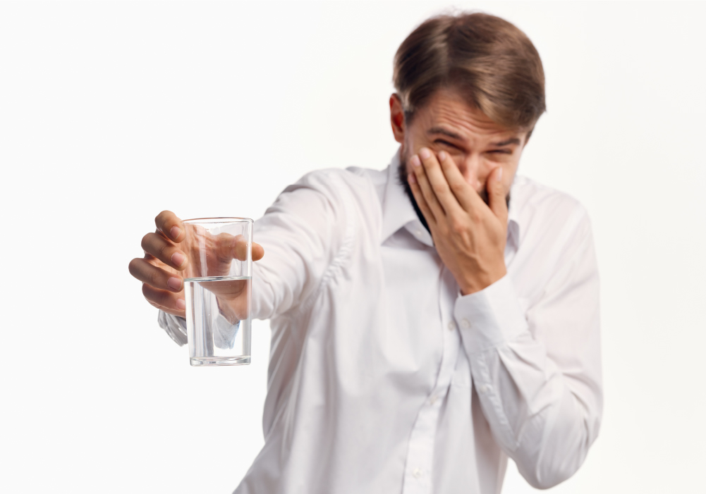 man plugging his nose at the scent of smelly water in a glass