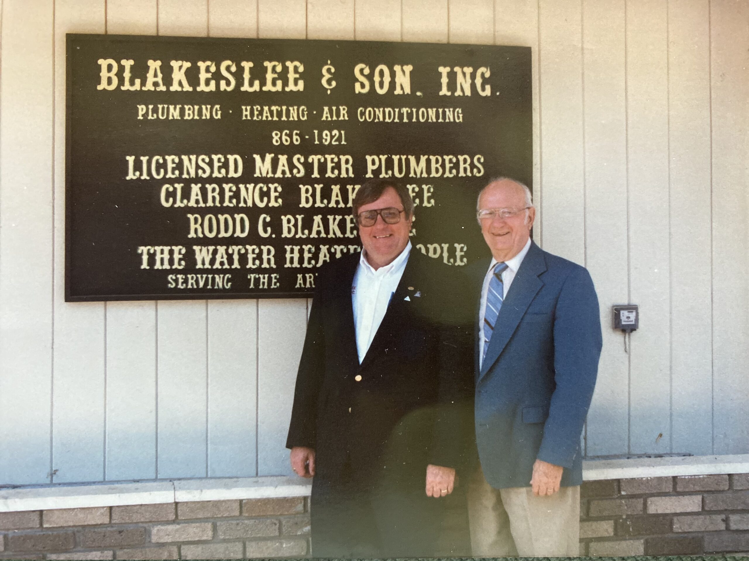 Blakeslee & Son founder Clarence Blakeslee and his son Rodd Blakeslee stand in front of the company's business sign.